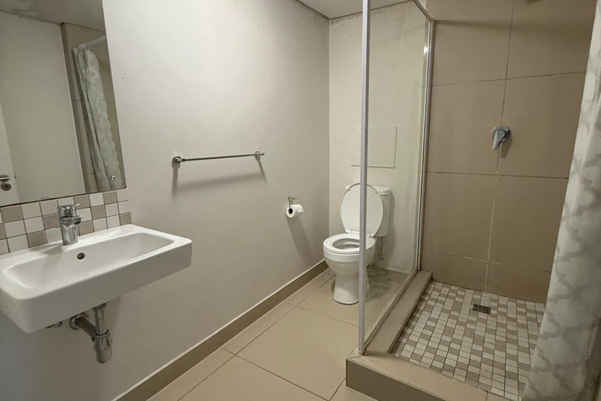 A functional bathroom featuring a wall-mounted basin, a tiled shower enclosure with a glass screen, and a toilet, showing signs of ceiling water damage.