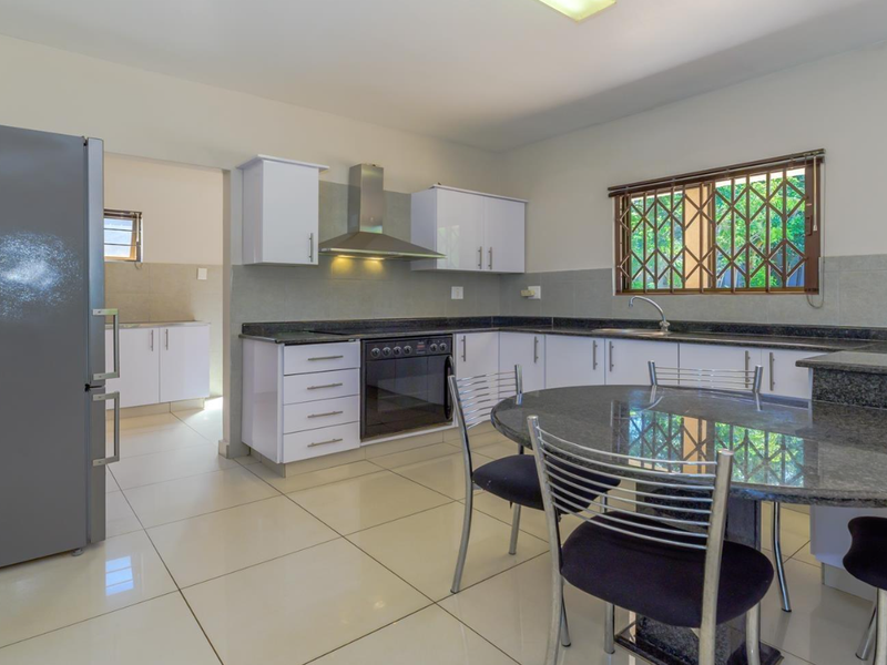 A functional kitchen featuring granite countertops, built-in cabinetry, a stainless steel extractor fan, and an integrated oven, with an adjoining scullery area.