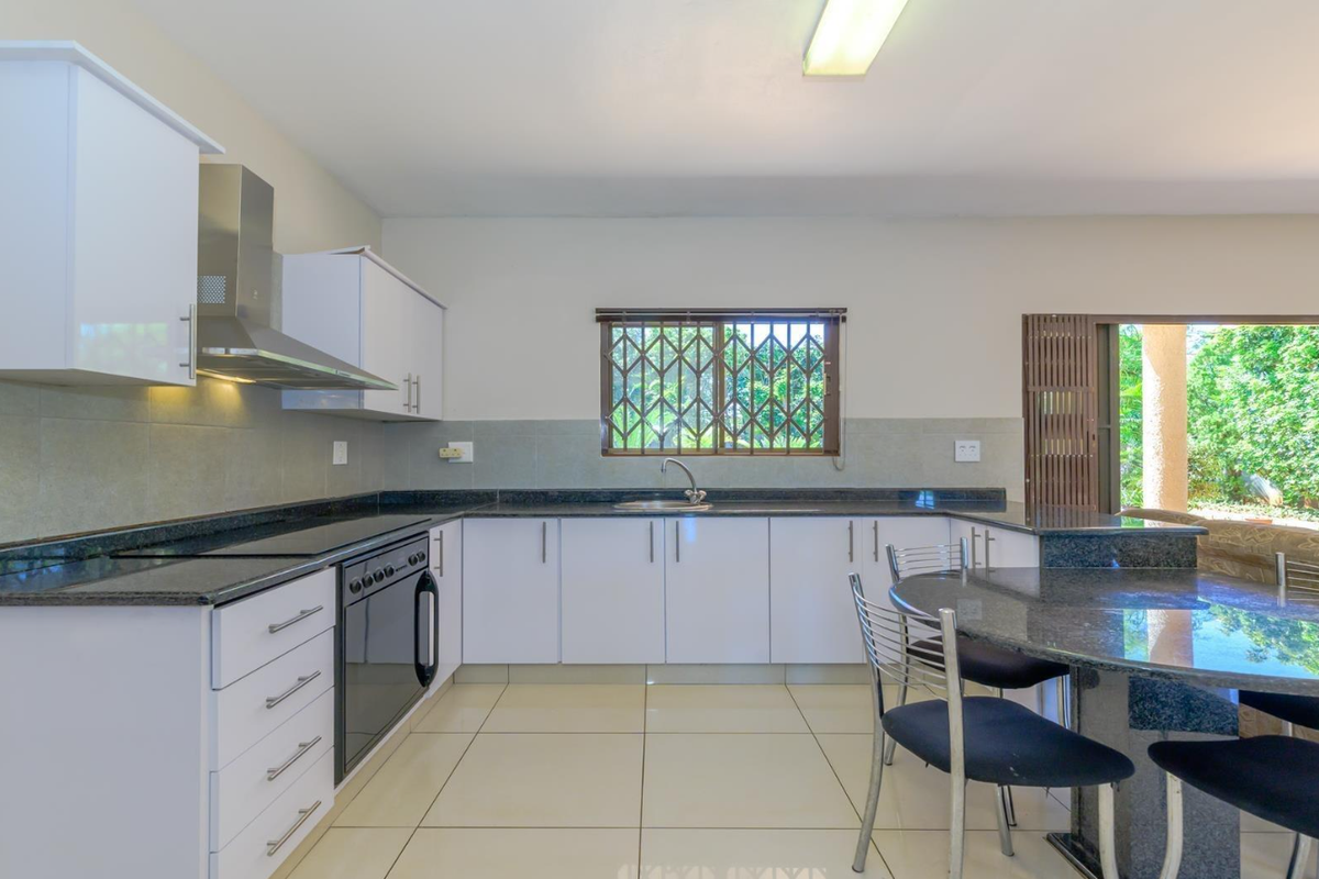 Modern kitchen featuring white cabinetry, granite countertops, built-in oven, and hob, with direct access to an outdoor patio area.