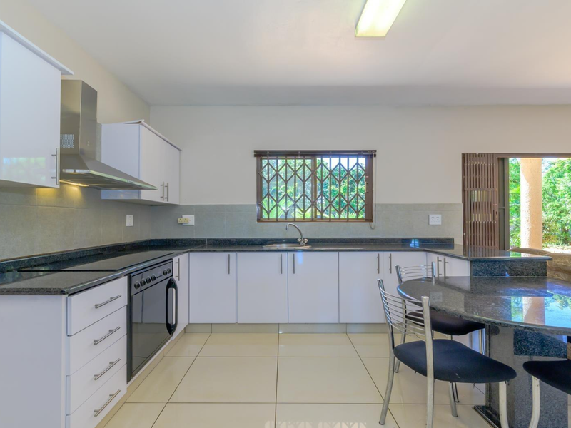 Modern kitchen featuring white cabinetry, granite countertops, built-in oven, and hob, with direct access to an outdoor patio area.