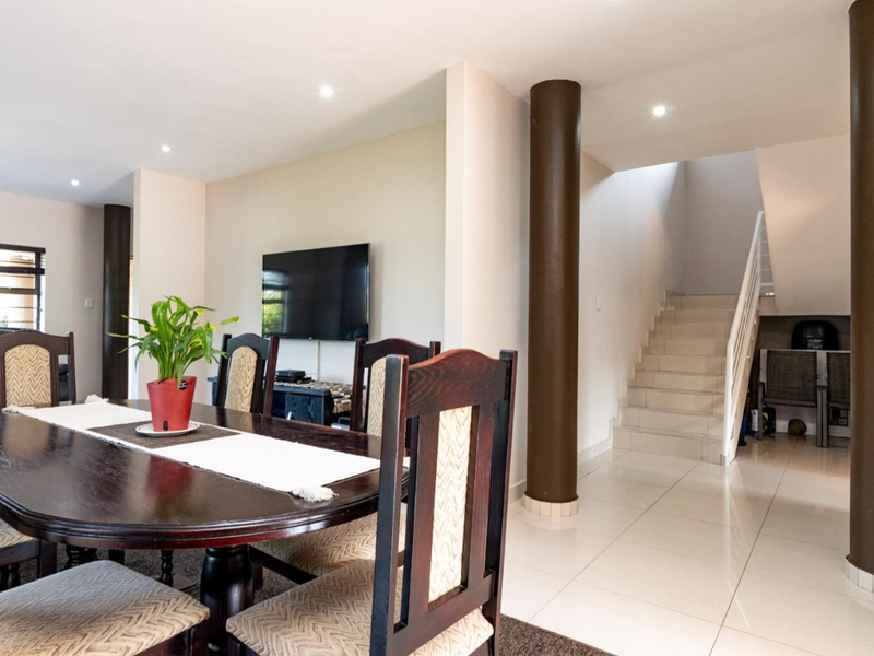 A dining area featuring tiled flooring, recessed lighting, and structural columns, with an adjacent staircase leading to the upper level.