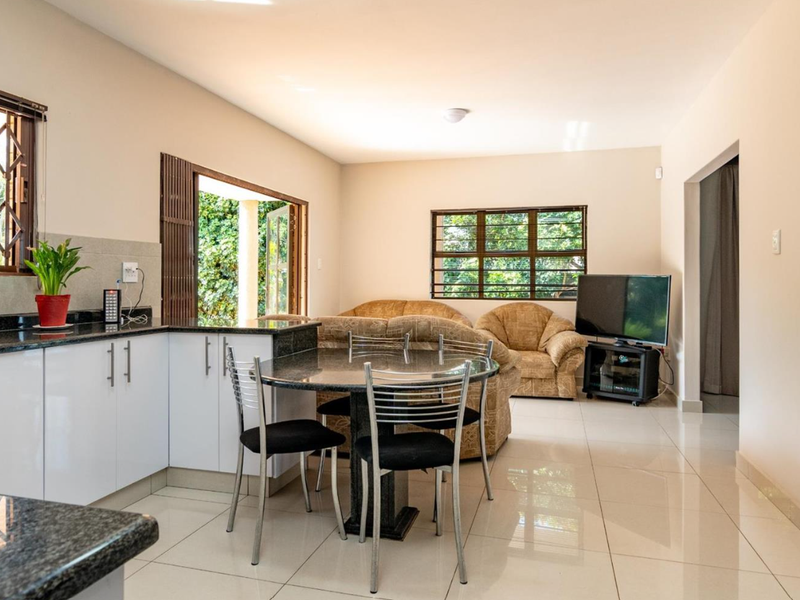Open-plan living and kitchen area featuring modern white cabinetry, granite countertops, tiled flooring, and direct access to the outdoor space.