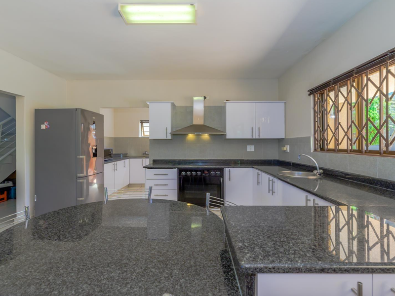 A functional kitchen featuring granite countertops, built-in cabinetry, a stainless steel oven with extractor fan, and a window with security bars.