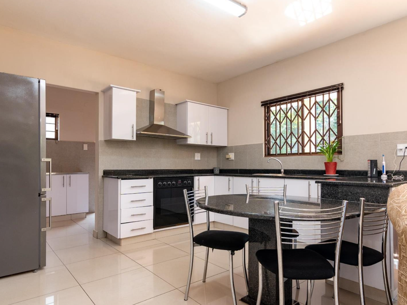 A functional kitchen featuring white cabinetry, granite countertops, a built-in oven with extractor fan, and tiled flooring, with an adjacent scullery area.