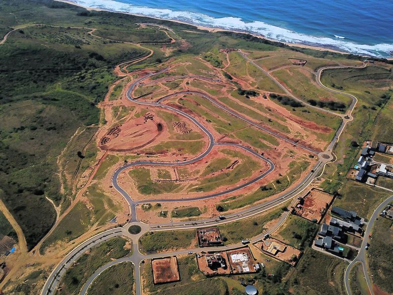 Aerial view of a residential development site featuring established paved roads, roundabouts, and proximity to the coastline.