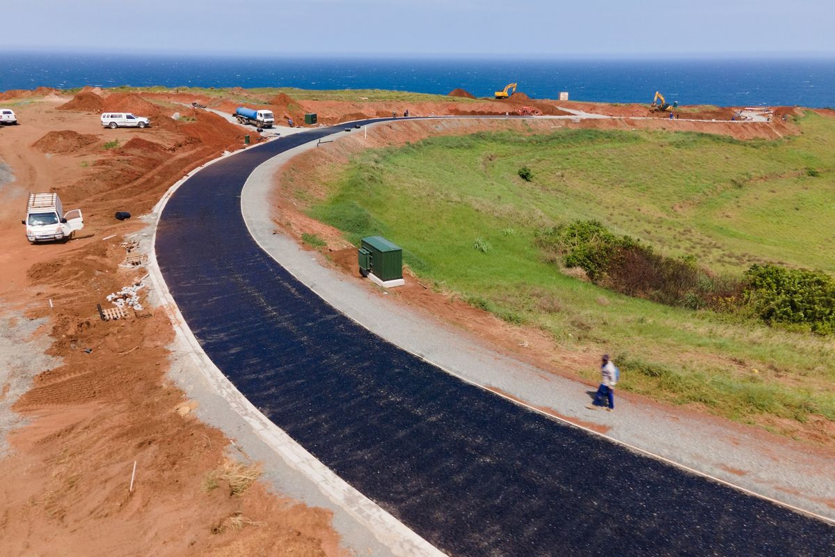Aerial view of a newly paved asphalt road under construction within a residential development, featuring ocean views and surrounding cleared land.