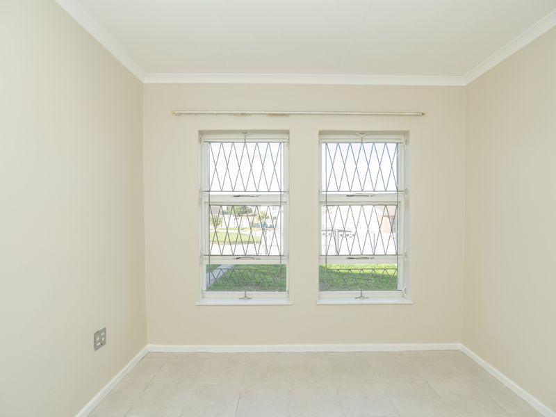 A clean, empty bedroom featuring neutral wall paint, tiled flooring, and windows fitted with security bars.