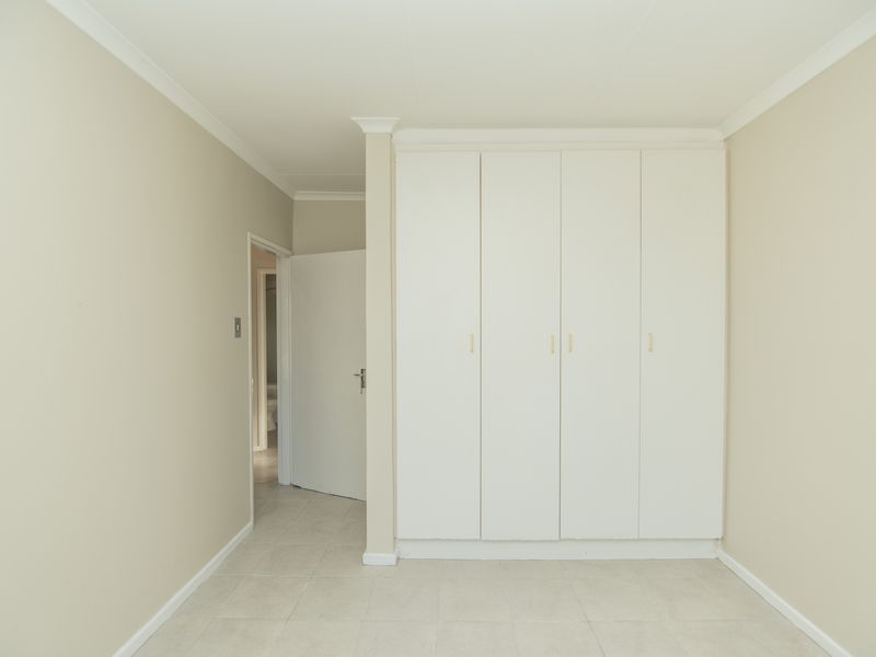 A clean, neutral bedroom featuring built-in cupboards and tiled flooring, offering a blank canvas for personalization.