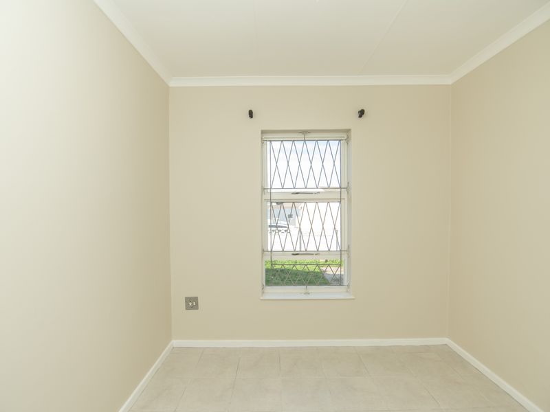 A clean, empty bedroom featuring neutral wall paint, tiled flooring, and a window fitted with security bars.