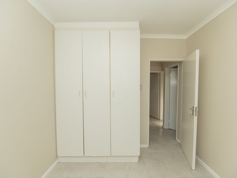 A clean, empty bedroom featuring neutral wall tones, tiled flooring, and built-in white cupboards, offering a versatile space ready for personalization.