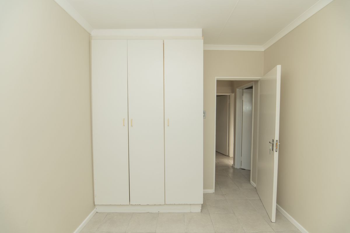 A clean, empty bedroom featuring neutral wall tones, tiled flooring, and built-in white cupboards, offering a versatile space ready for personalization.