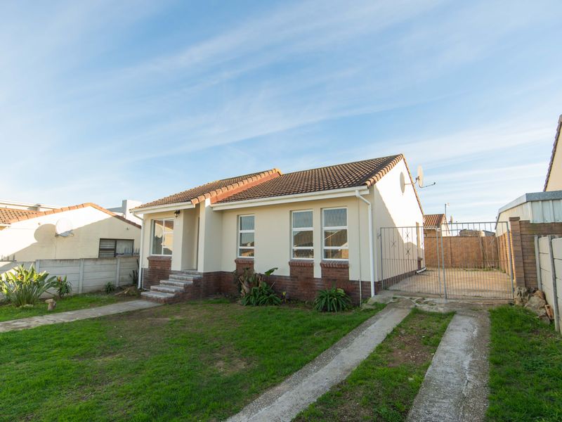 Front view of a single-story residential house featuring a tiled roof, brick base detailing, a concrete driveway, and a gated side entrance.