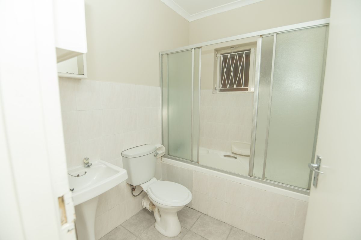 A functional bathroom featuring a pedestal basin, toilet, and a bathtub with a sliding shower screen, finished with neutral wall and floor tiles.
