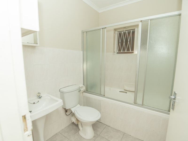 A functional bathroom featuring a pedestal basin, toilet, and a bathtub with a sliding shower screen, finished with neutral wall and floor tiles.