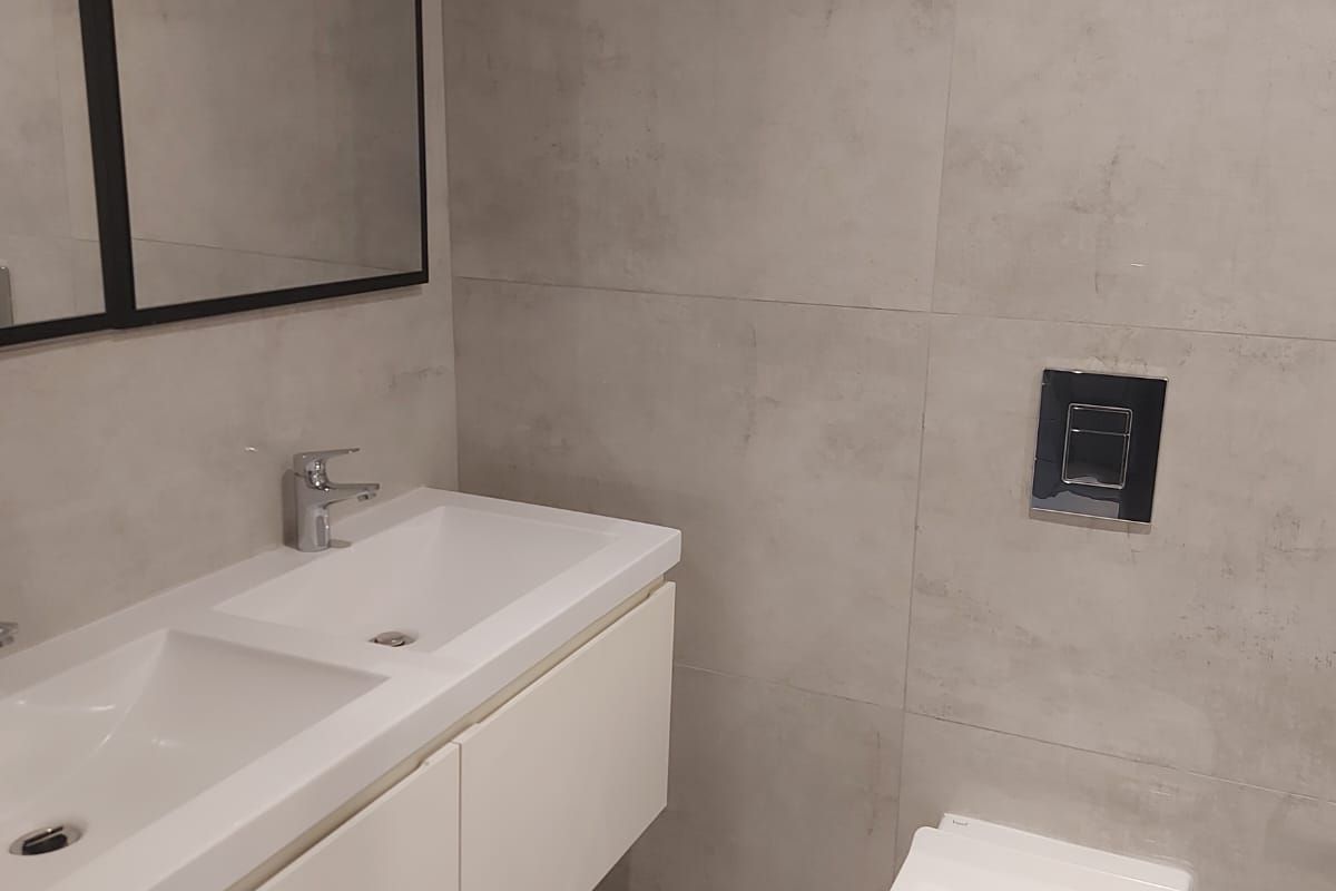Modern bathroom featuring a sleek wall-mounted double vanity, wall-hung toilet with concealed cistern, and contemporary large-format grey tiling.