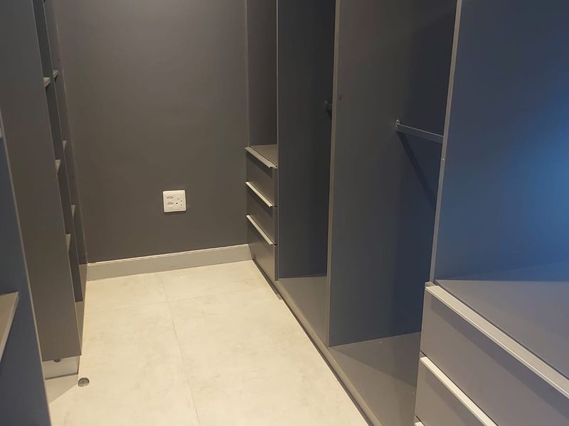A modern walk-in closet featuring dark grey built-in cabinetry with ample shelving and drawer storage, complemented by light-toned tiled flooring.
