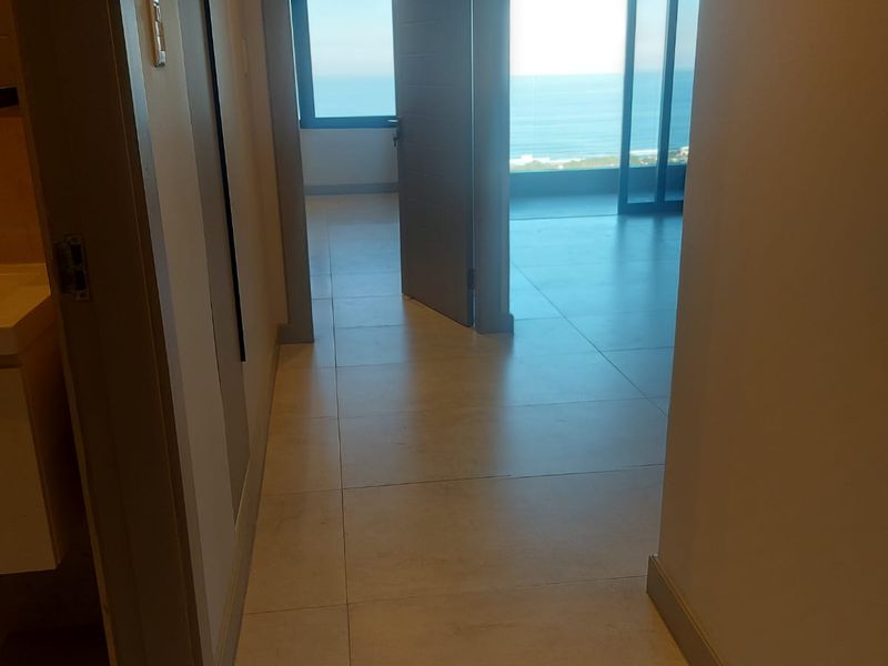 A bright, modern hallway with neutral tiled flooring leading towards an open-plan living area with expansive ocean views.