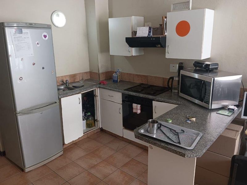 A compact kitchen featuring laminate countertops, built-in cabinetry, an electric hob, and an oven, with tiled flooring and backsplash throughout.
