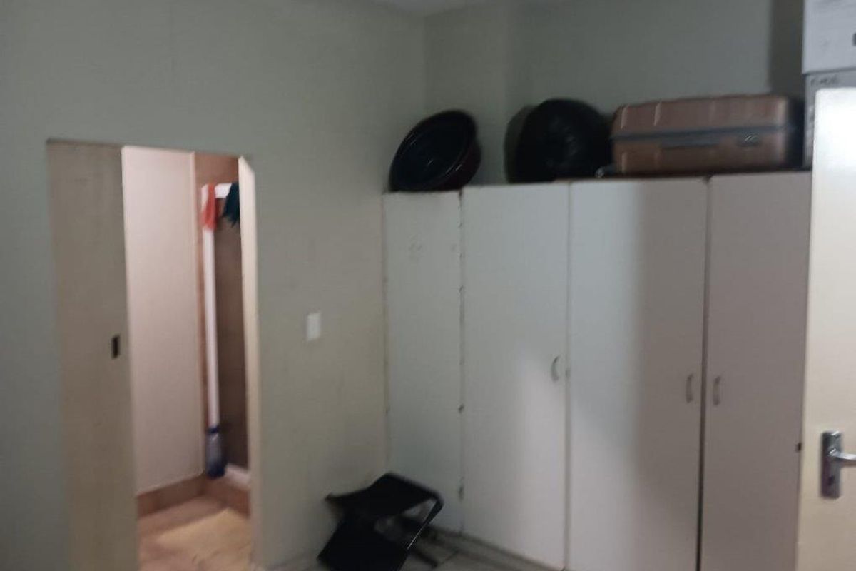 A bedroom featuring built-in cupboards and a doorway leading to an adjacent space, requiring cosmetic updates to improve the overall finish.