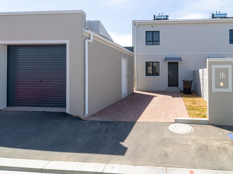 Front view of a modern townhouse featuring a paved driveway, single garage with roller door, and solar water heating system on the roof.