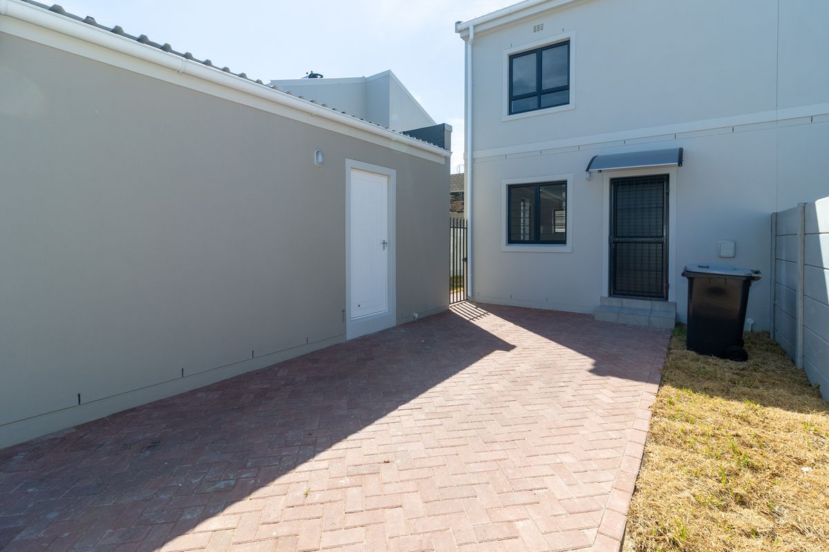 Rear exterior view of the townhouse featuring a paved courtyard area, security door, and boundary wall.