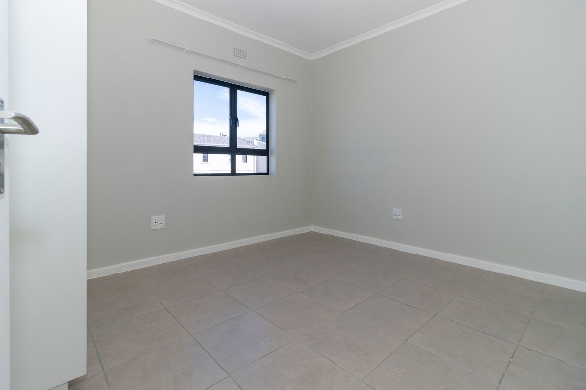A clean, empty bedroom featuring neutral tiled flooring, modern aluminium window frames, and crisp white walls, ready for personalization.