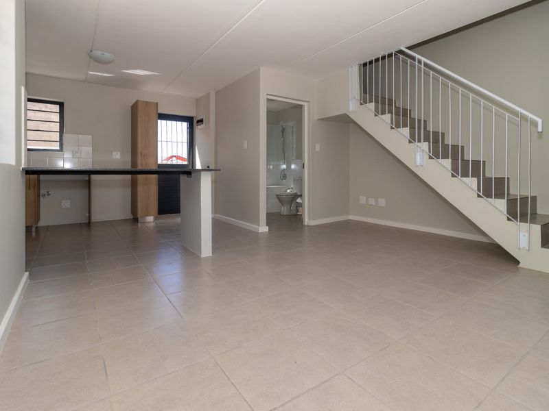 An open-plan living and kitchen area featuring tiled floors, a staircase with a metal balustrade, and direct access to a ground-floor bathroom.