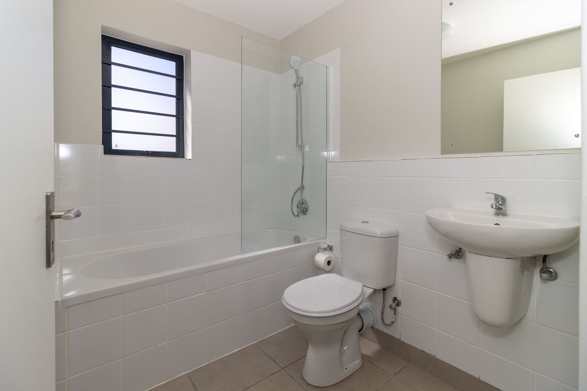 A clean and functional bathroom featuring a bathtub with a glass shower screen, a pedestal basin, and a toilet with neutral wall tiling.