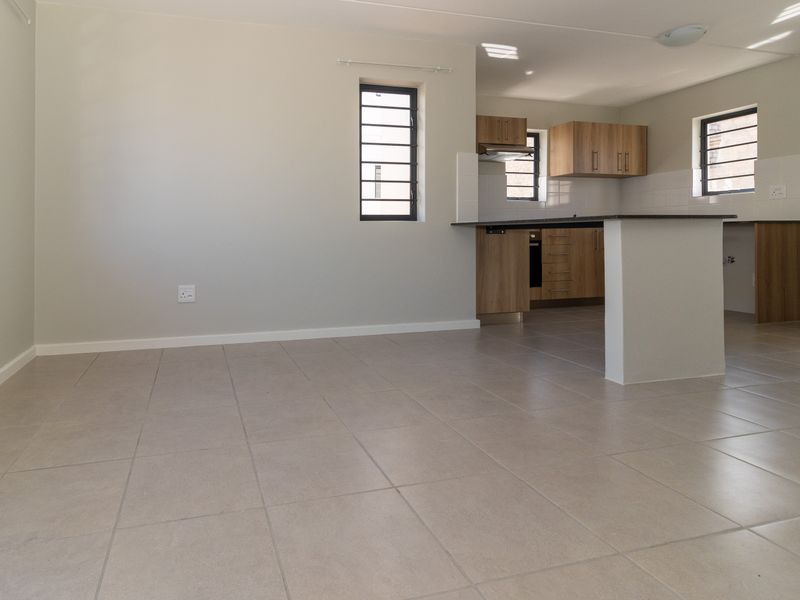 An open-plan living and kitchen area featuring neutral tiled flooring, modern wood-finish cabinetry, a kitchen island, and secure window bars.