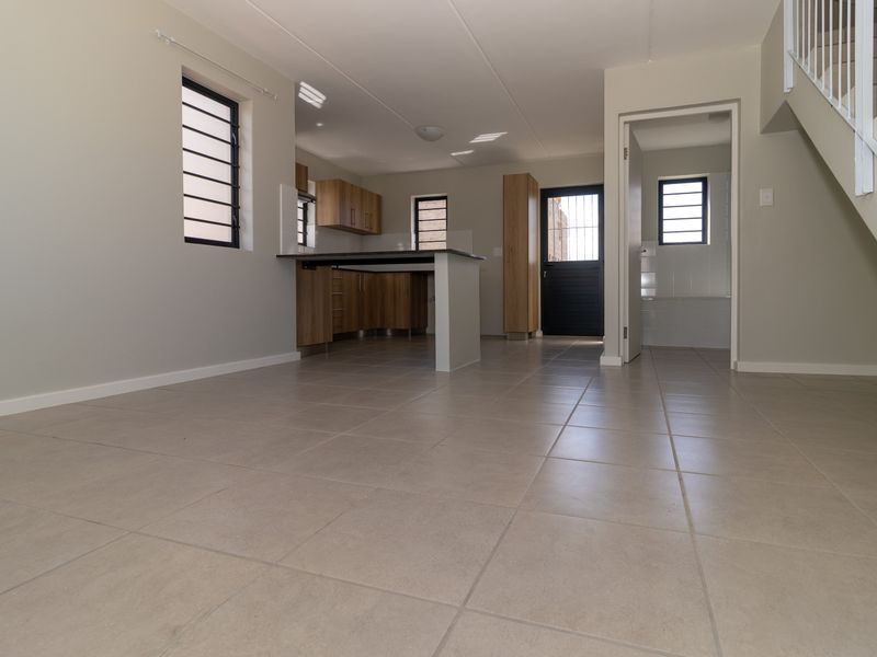 Open-plan living and kitchen area featuring neutral tiled flooring, modern wood-finish cabinetry, and a staircase leading to the upper level.
