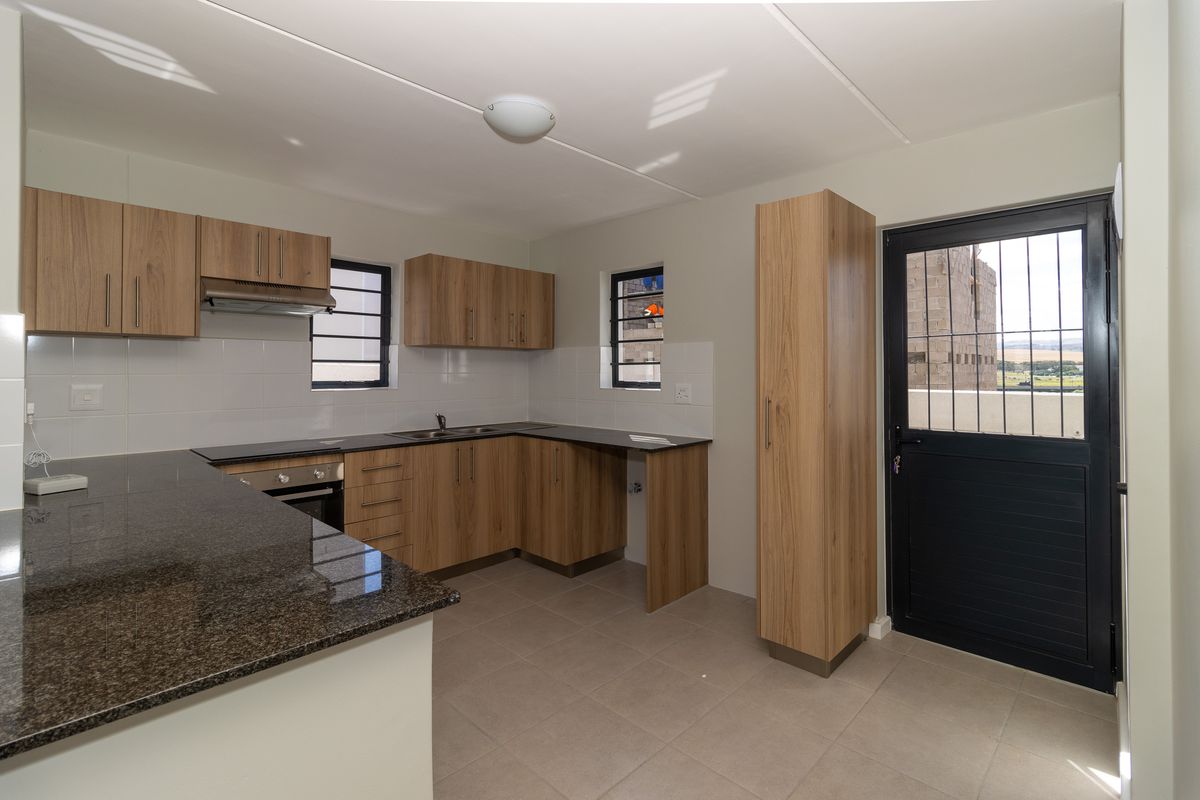 Modern kitchen featuring wood-finish cabinetry, granite countertops, built-in oven, extractor fan, and tiled flooring with direct access to the exterior.