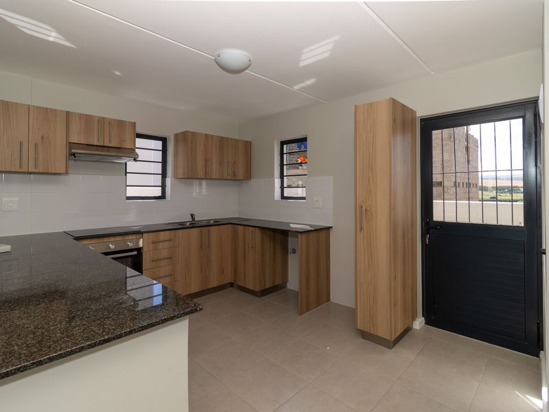 Modern kitchen featuring wood-finish cabinetry, granite countertops, built-in oven, extractor fan, and tiled flooring with direct access to the exterior.