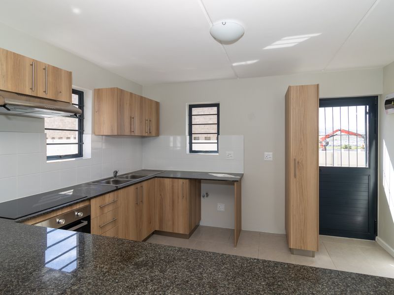 Modern kitchen featuring light wood cabinetry, granite countertops, built-in oven and hob, tiled backsplash, and direct access to the exterior.