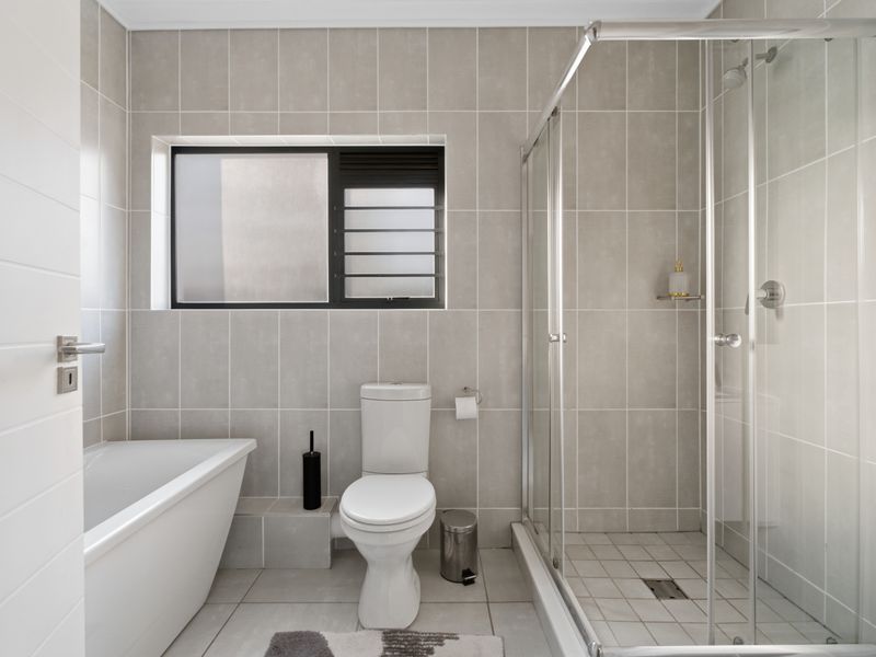 Modern bathroom featuring a freestanding bathtub, a separate glass-enclosed shower, and neutral floor-to-ceiling tiling.