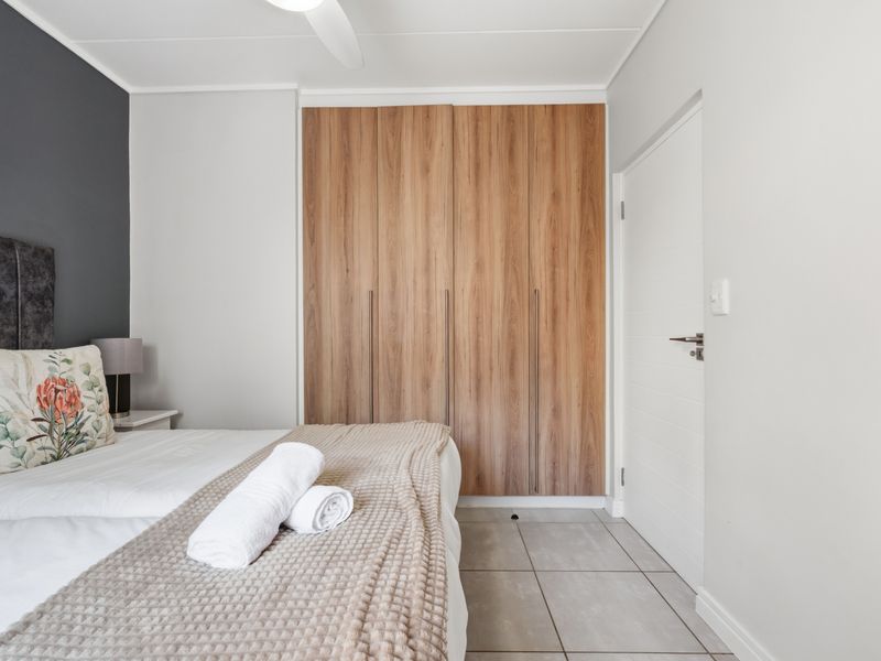 A well-maintained bedroom featuring modern wood-finish built-in cupboards, neutral tiled flooring, and a ceiling fan, offering a clean and functional living space.