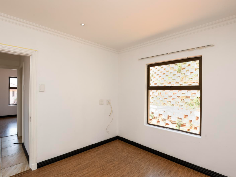 An empty bedroom featuring laminate flooring, recessed downlighting, and a window overlooking a retaining wall. The space is ready for personalization.