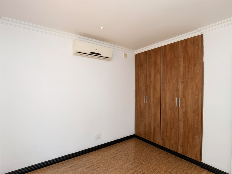 A clean, empty bedroom featuring wood-look laminate flooring, built-in wooden cupboards, and a wall-mounted air conditioning unit.