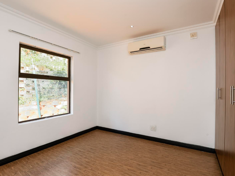 A clean, empty bedroom featuring laminate flooring, built-in wooden wardrobes, and a wall-mounted air conditioning unit.