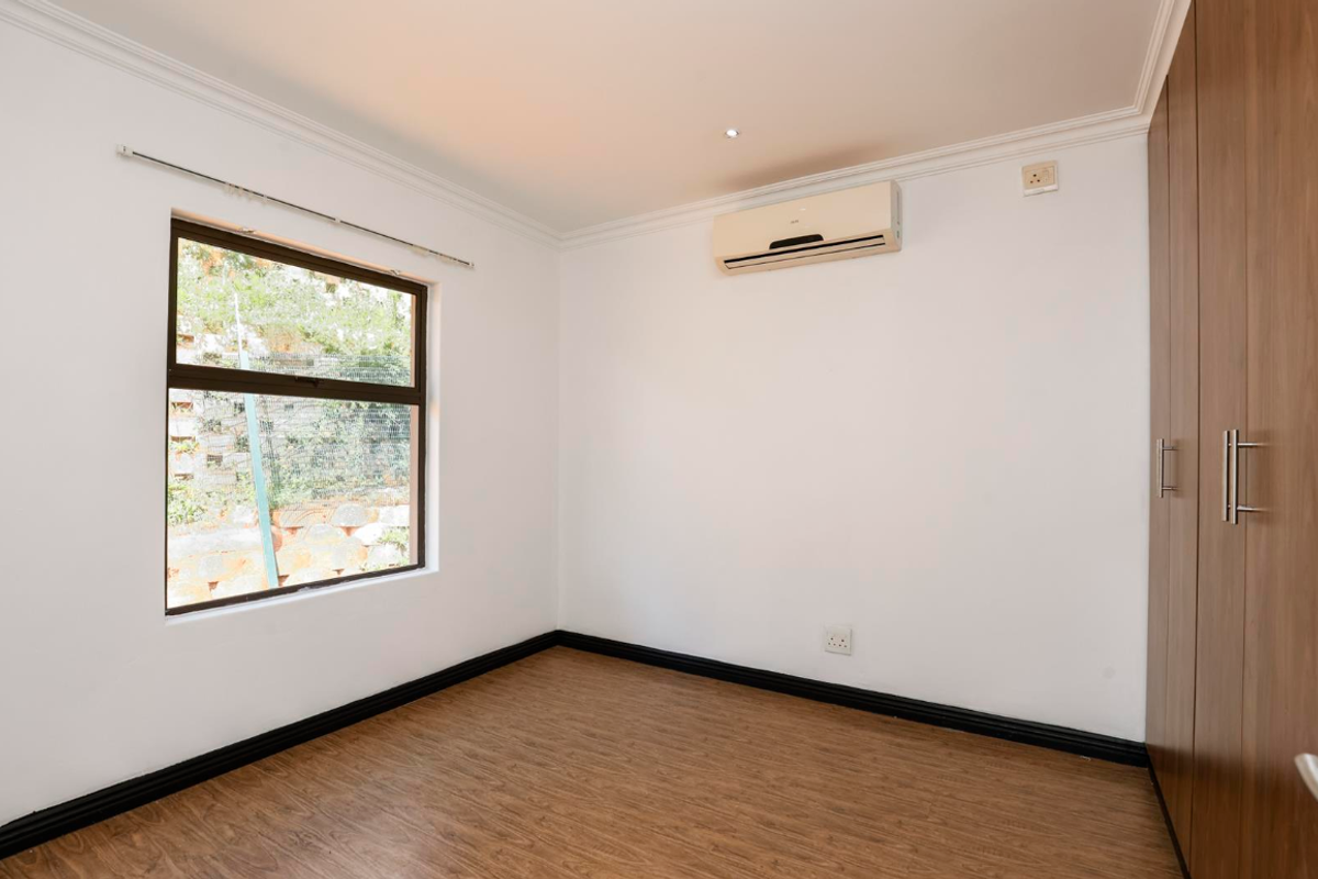 A clean, empty bedroom featuring laminate flooring, built-in wooden wardrobes, and a wall-mounted air conditioning unit.