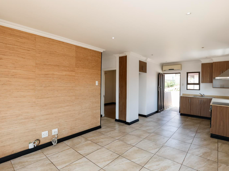 An open-plan living and kitchen area featuring tiled floors, a wood-look feature wall, modern cabinetry, and an integrated extractor fan.