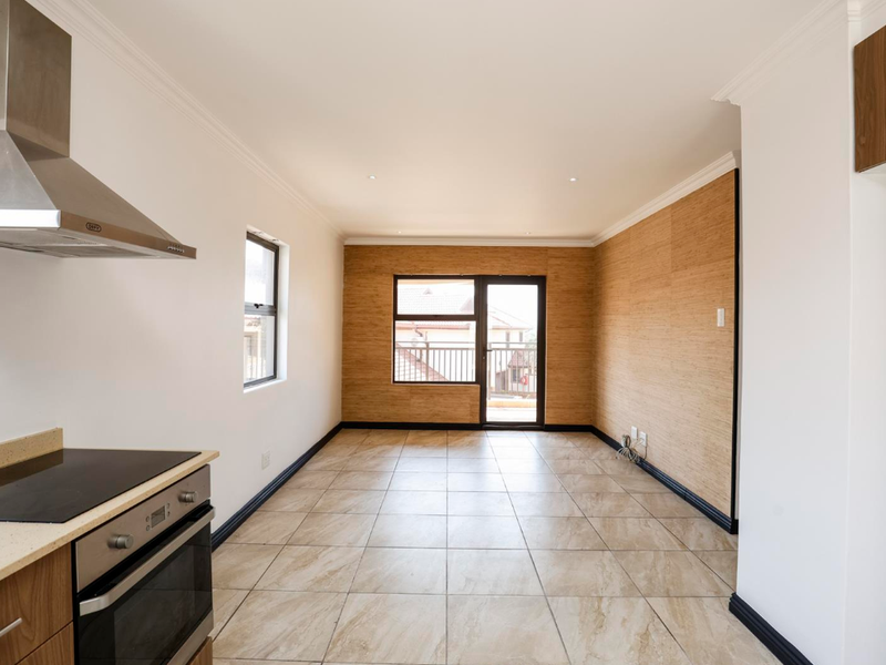 An open-plan kitchen and living area featuring tiled floors, wood-look wall paneling, built-in oven and hob, and a sliding door leading to a balcony.