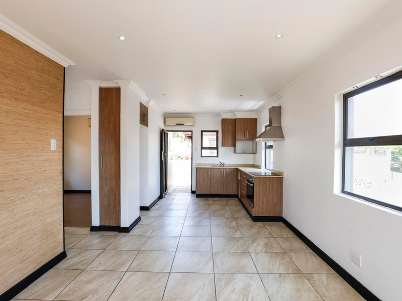 An open-plan kitchen and living area featuring modern wood-finish cabinetry, tiled flooring, recessed lighting, and an integrated air conditioning unit.