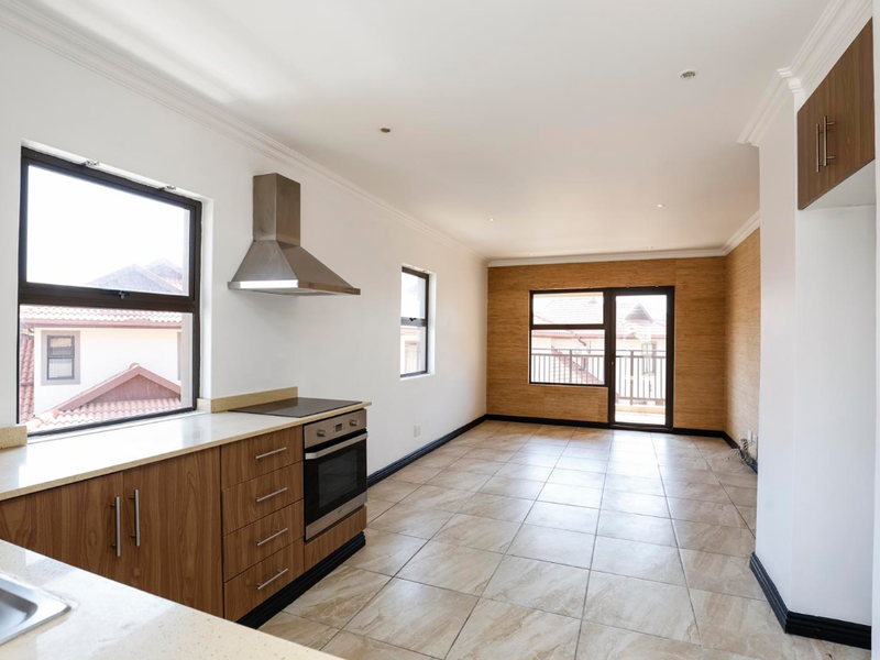 Spacious open-plan kitchen and living area featuring modern wood-finish cabinetry, stone countertops, built-in appliances, tiled flooring, and access to a private balcony.