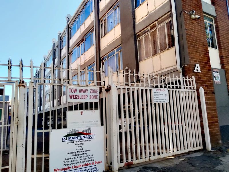 Front exterior view of a multi-story apartment building featuring a gated entrance, brick facade, and metal window frames.