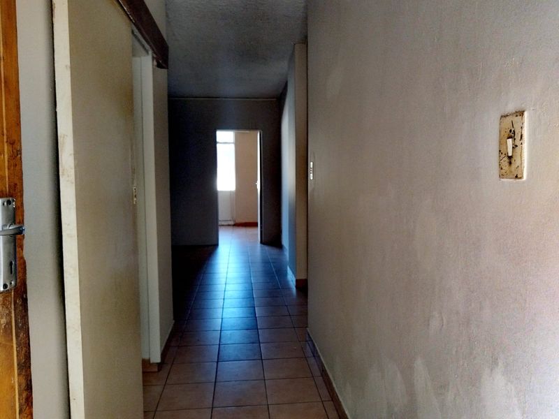 A vacant hallway featuring tiled flooring and dated wall finishes, requiring cosmetic updates to improve the overall aesthetic.