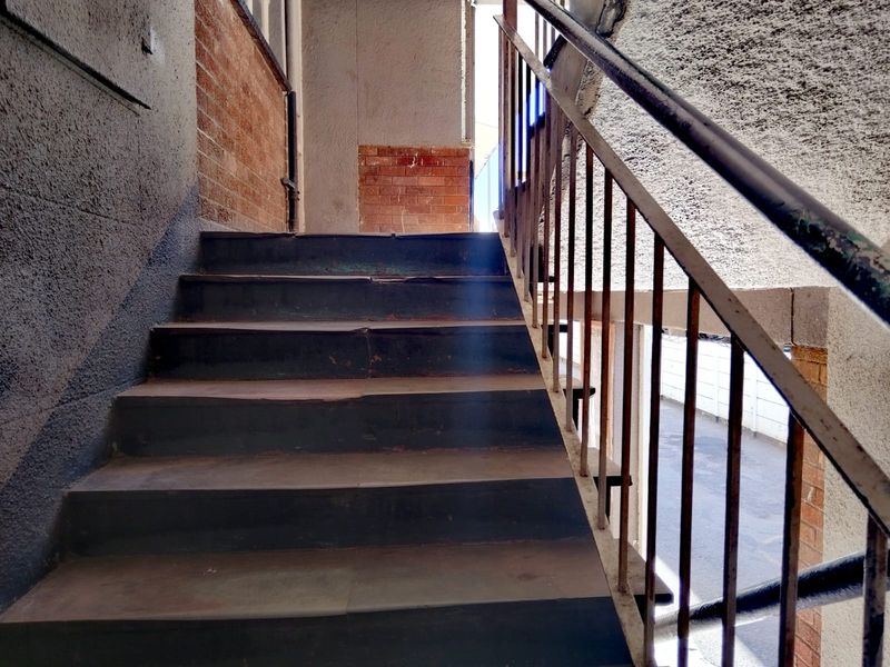 An exterior concrete staircase with metal handrails, showing significant signs of wear and weathering on the steps and structural finishes.