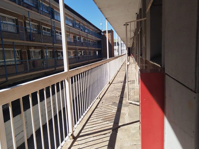 An exterior walkway or balcony area featuring stone paving, a metal balustrade, and a wall-mounted fire hose cabinet in an apartment complex setting.