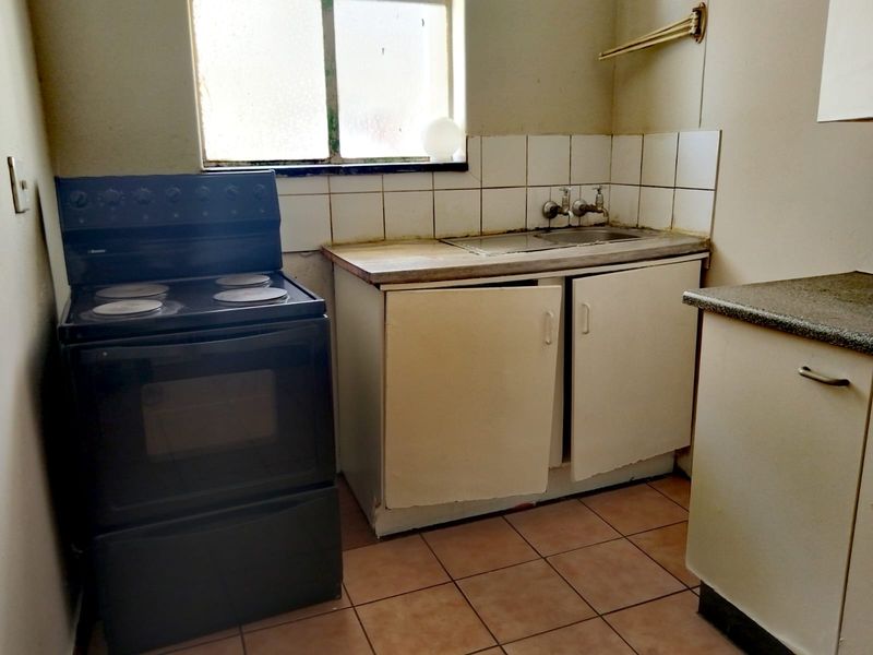 A dated kitchen featuring a freestanding electric stove, stainless steel sink, tiled splashback, and worn cabinetry requiring renovation.