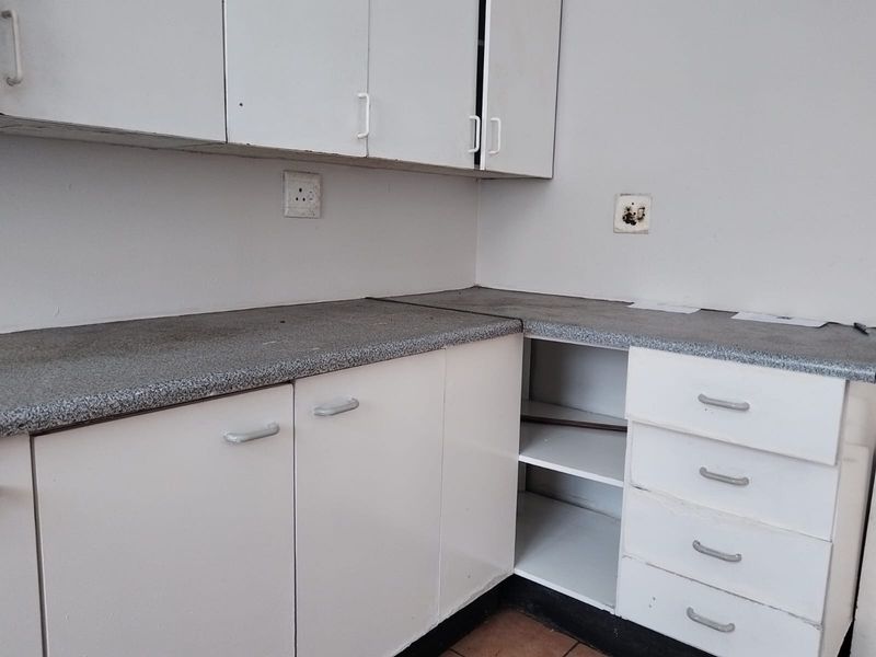 A dated kitchen area featuring white cabinetry, laminate countertops, and built-in drawers, currently vacant and in need of cosmetic updates.