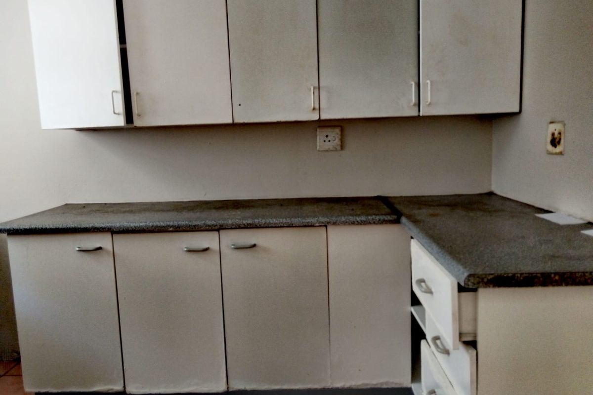 A dated kitchen area featuring built-in cabinetry, laminate countertops, and integrated drawer storage, requiring cosmetic updates to improve its overall aesthetic and functionality.